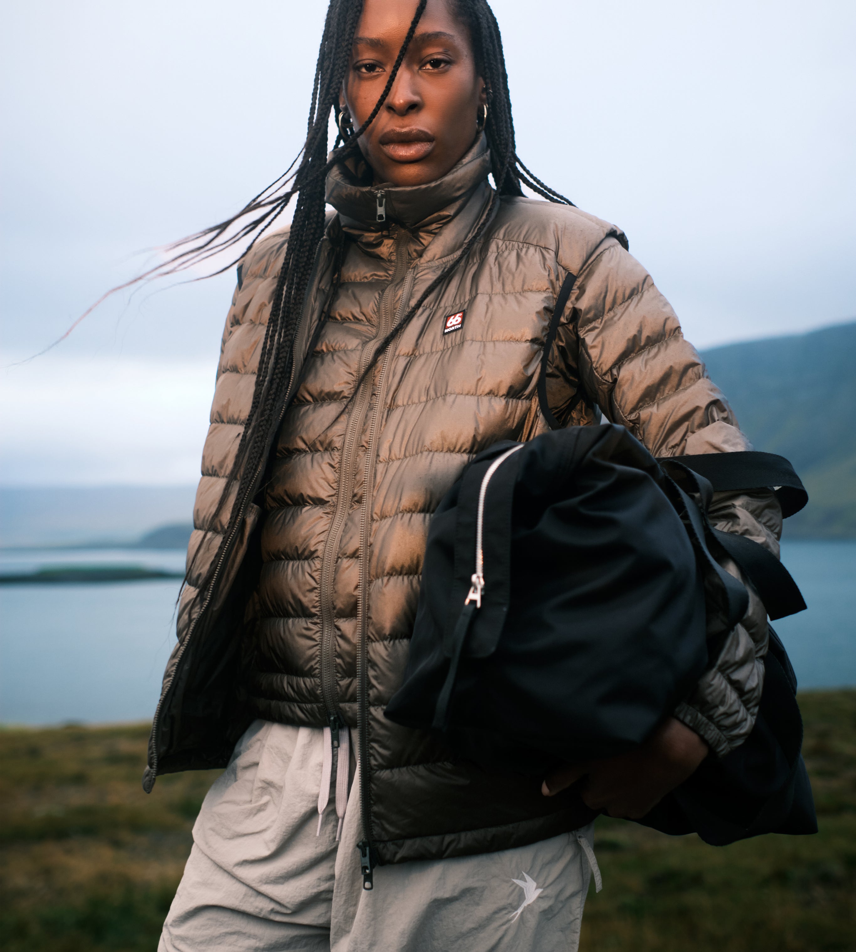 Person wearing a puffer jacket and holding a bag with a scenic background