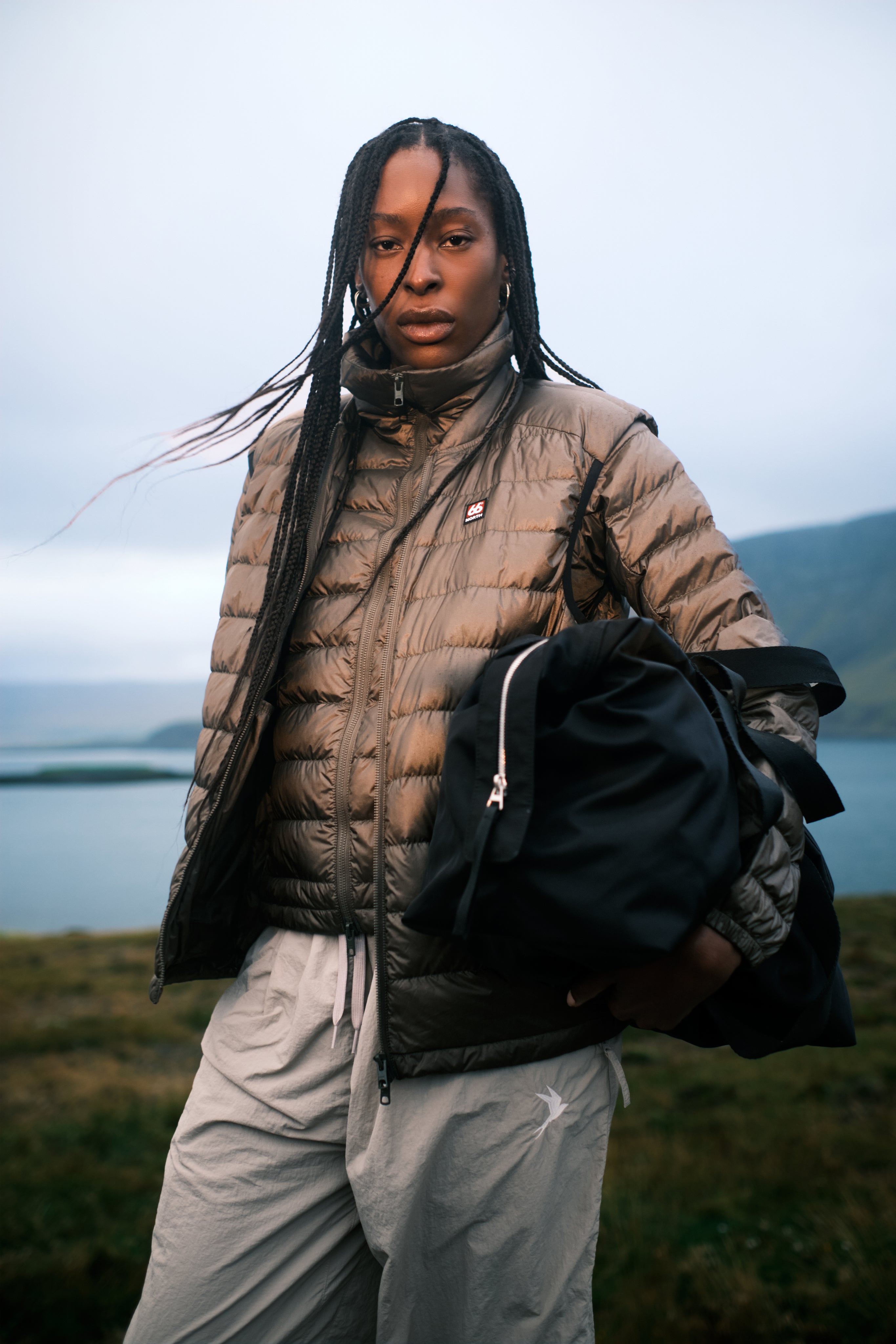 Person wearing a puffer jacket and holding a bag with a scenic background