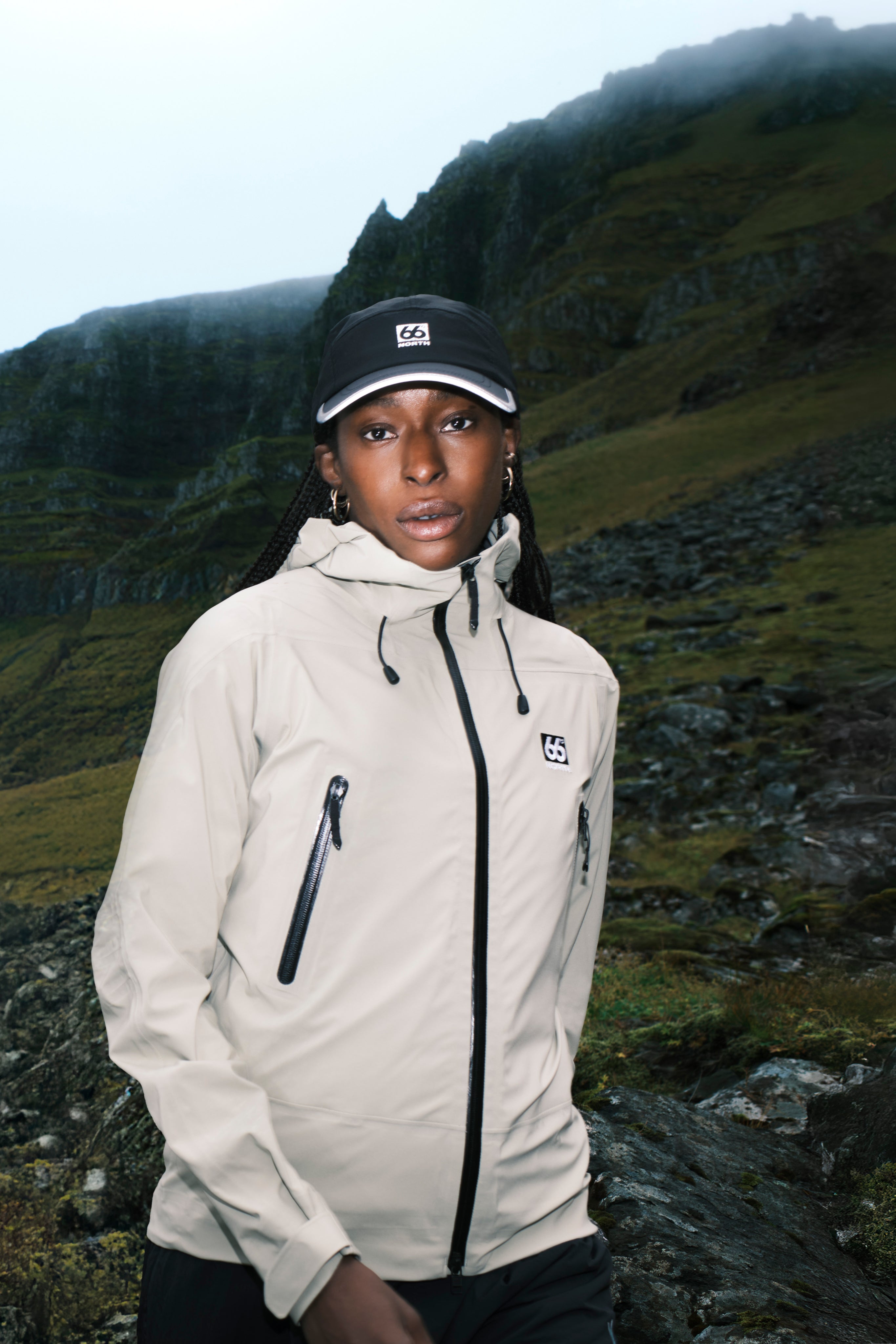 Person wearing a beige jacket and black cap in a mountainous landscape