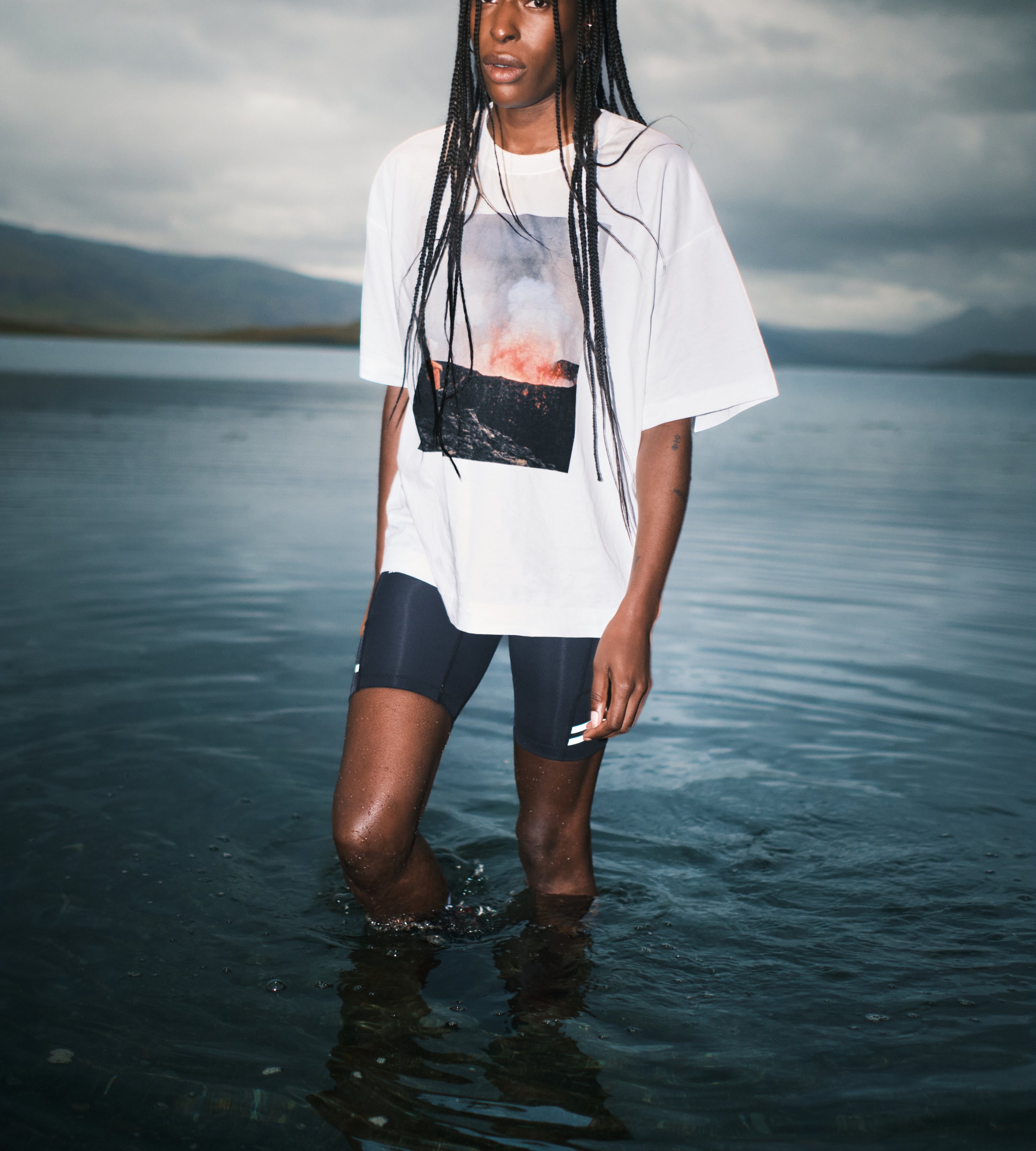 Person standing in water wearing a white t-shirt with a graphic design and dark shorts.