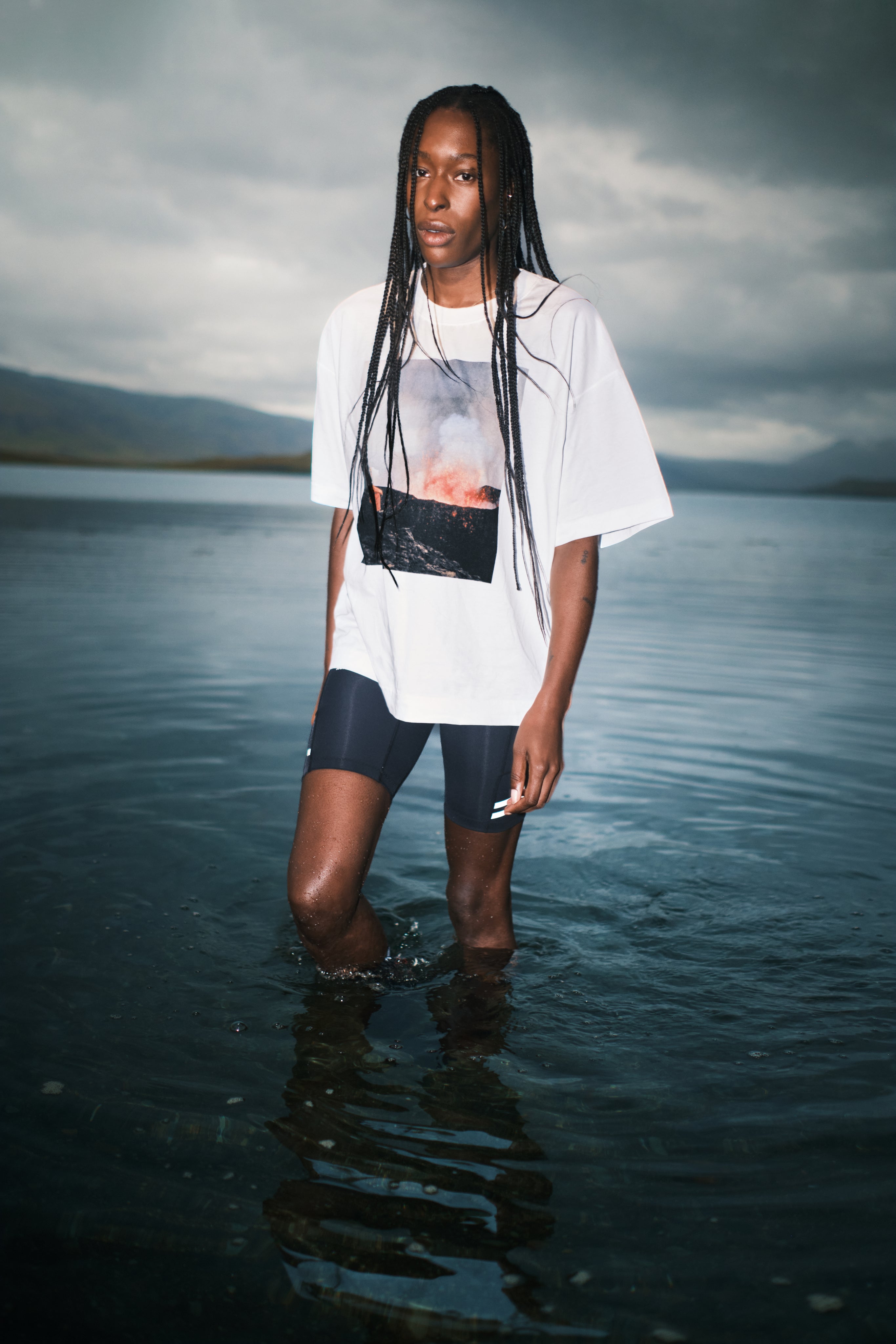 Person standing in water wearing a white t-shirt with a graphic design and dark shorts.