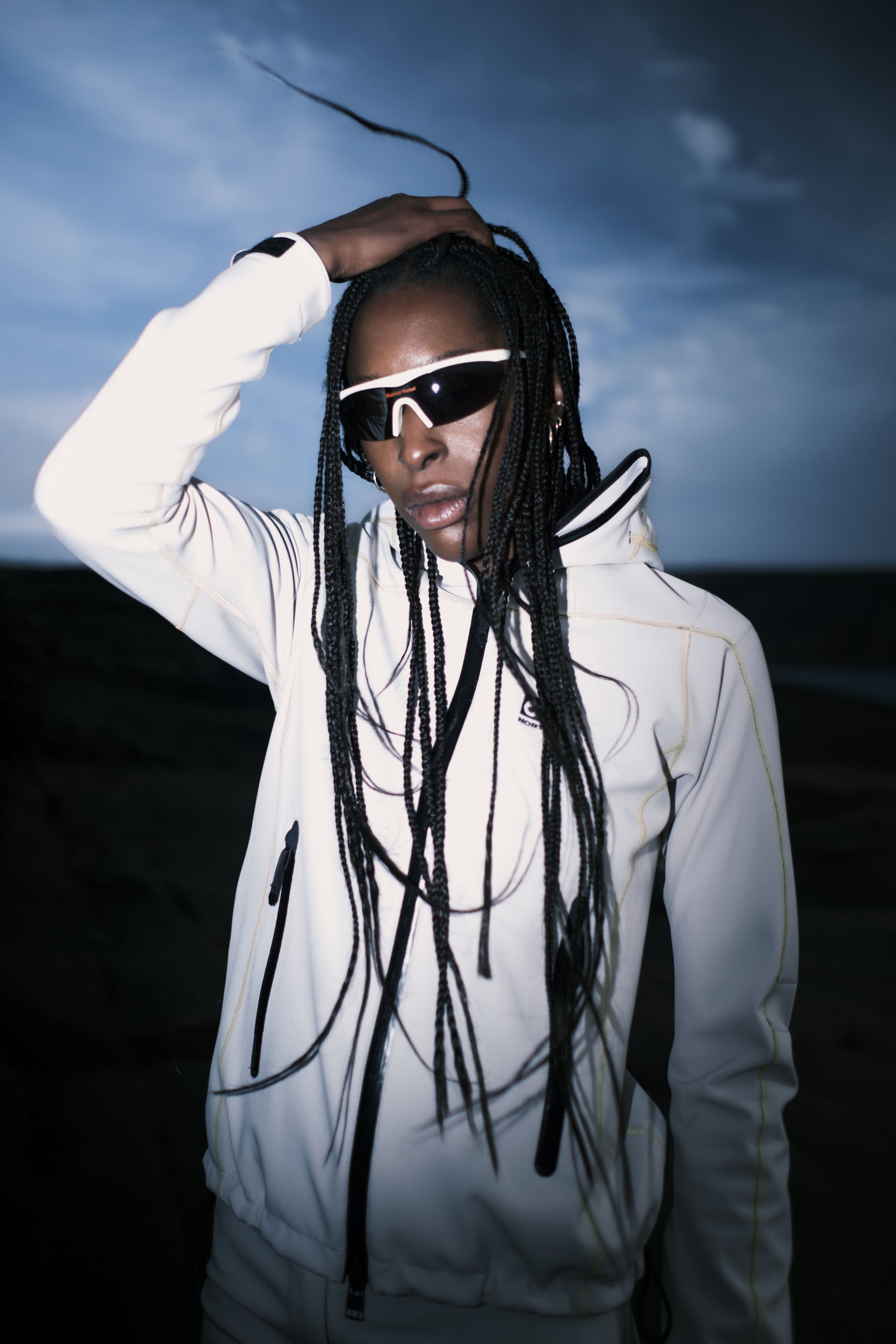 Person wearing a white outfit with reflective sunglasses against a dark background