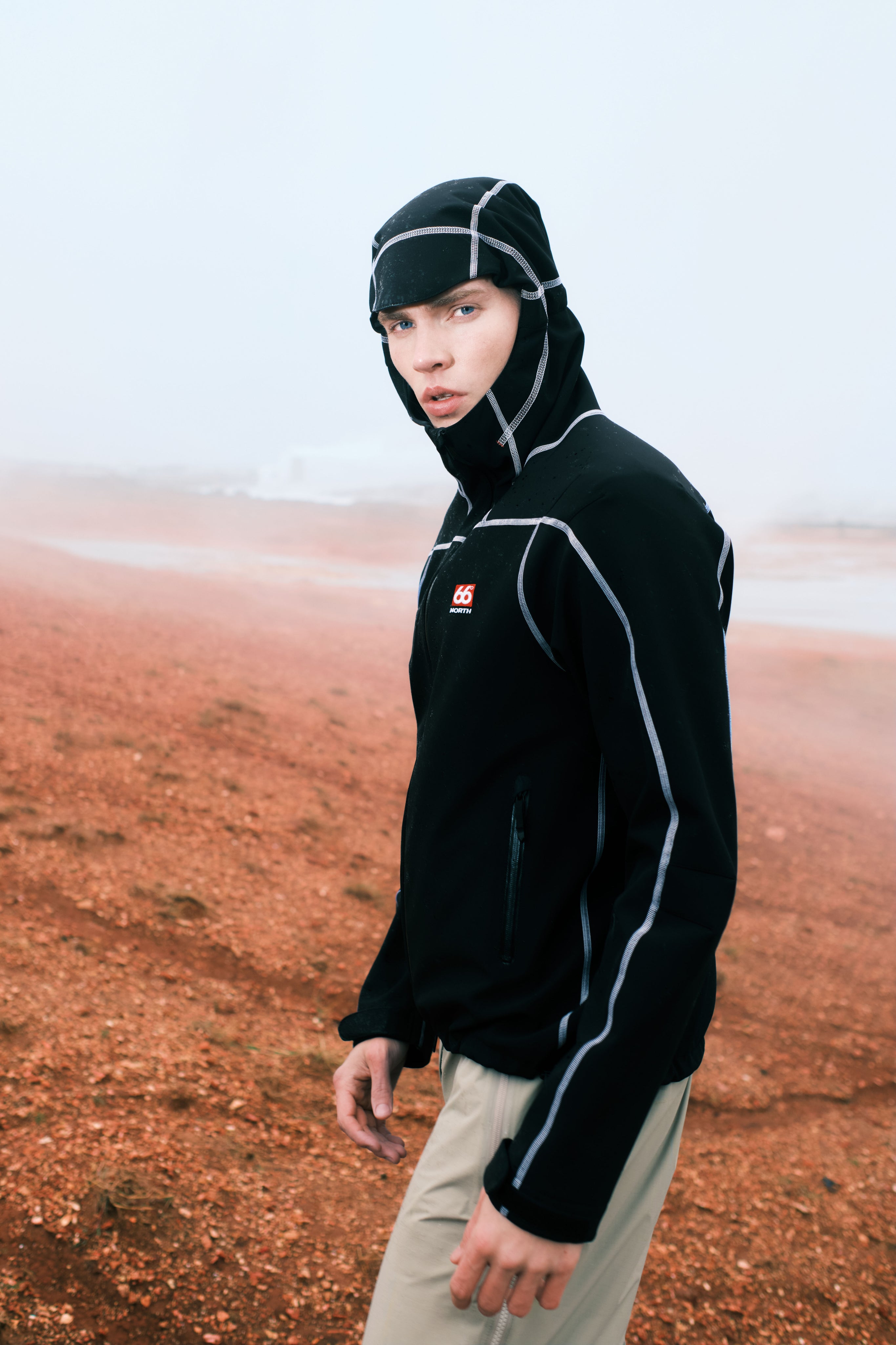 Person wearing a black hoodie with a logo in a desert-like setting